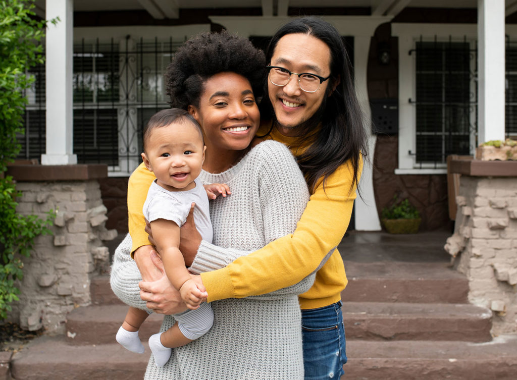 diverse mother and father with baby standing outside of their home, happy with their homeowners insurance collinsville illinois